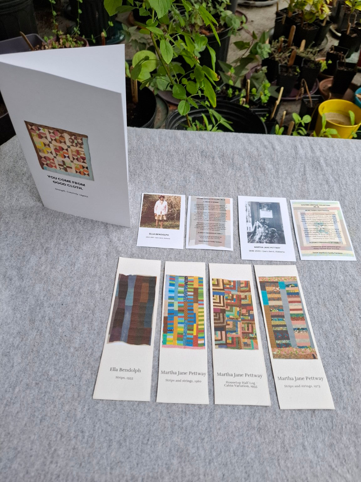 Gee's Bend quilt bookmarks arranged with other family heritage keepsakes on a tabletop, photographed outdoors.