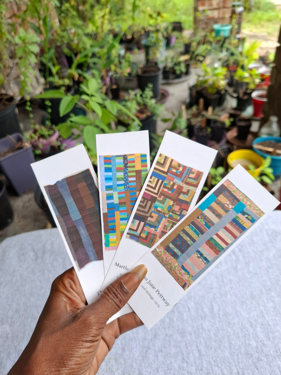Four Gee's Bend Quilters Legacy bookmarks held in my hand at Sweet Martha's Family Farmacy, featuring quilts by Ella Bendolph and Martha Jane Pettway.