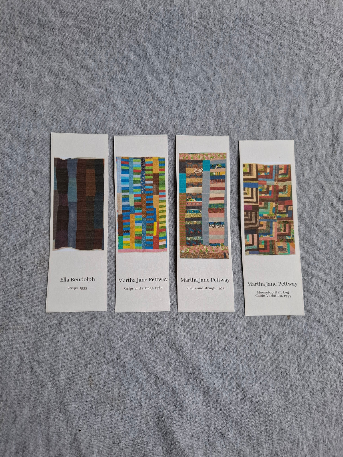 Four Gee's Bend Quilters Legacy bookmarks displayed side by side with quilt artwork fronts facing up on gray fabric.