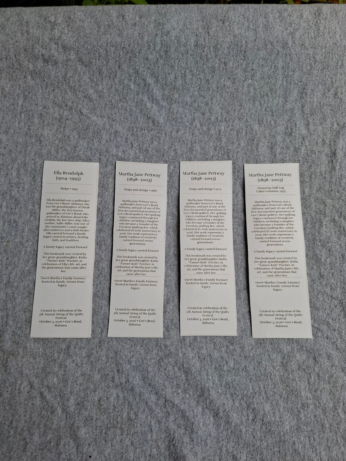 Four Gee's Bend Quilters Legacy bookmarks displayed together with their biography backs facing up on gray fabric.